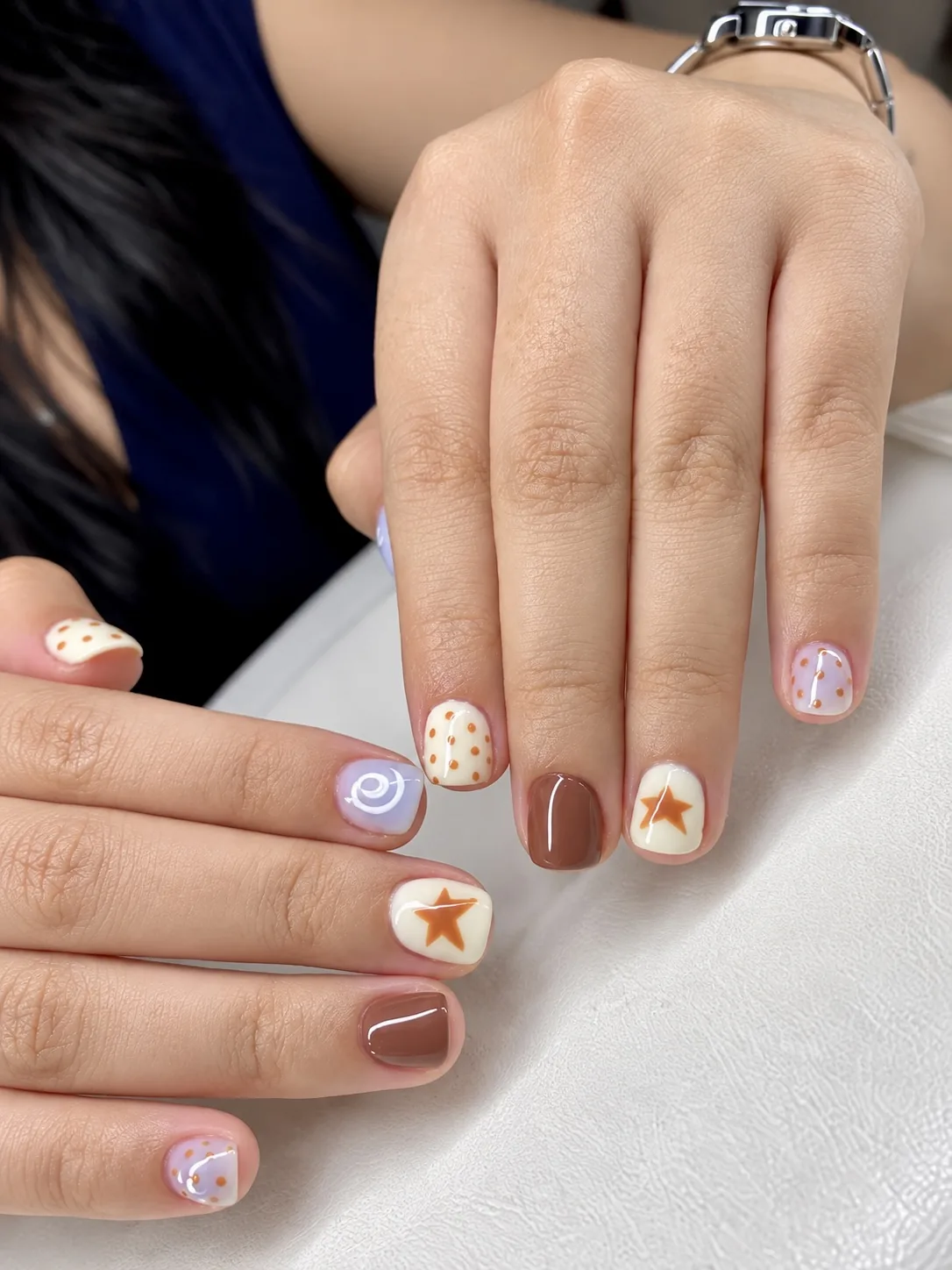 Short nails with hand-painted stars, polka dots and a swirl in cream, brown and lilac by Dan at AyuriNails Beauty Lounge